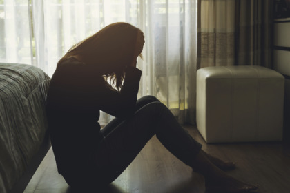 Kobieta zmaga się z depresją. Siedzi na podłodze przy łóżku